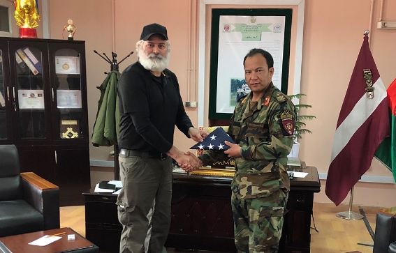 Al Santos standing with a miliarty member shaking hands and holding a folded American flag