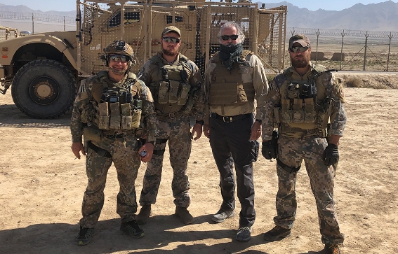 Al Santos wearing a bulletproof vest with three military members standing in front of a military vehicle