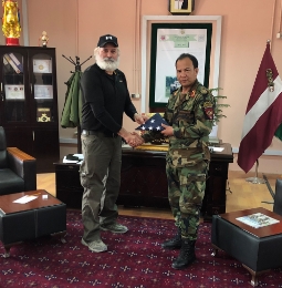 Al Santos de pie con un miembro de la milicia dándose la mano y sosteniendo una bandera americana doblada