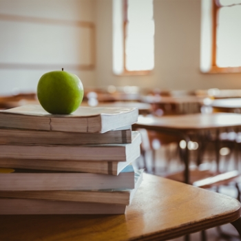 A stack of books with an apple on top in a classroom